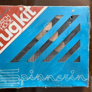 May include: A blue and white rug kit with the text "Rug Kit" and "Latch Hook" on the front. The kit includes yarn, a canvas, and a latch hook tool.