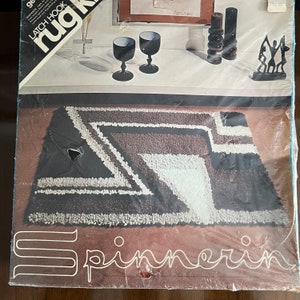 May include: A brown and white rug kit with the text "rug hook latch hook" and "Spinnerin" on the packaging. The rug kit features a geometric design with black, white, and brown yarn.