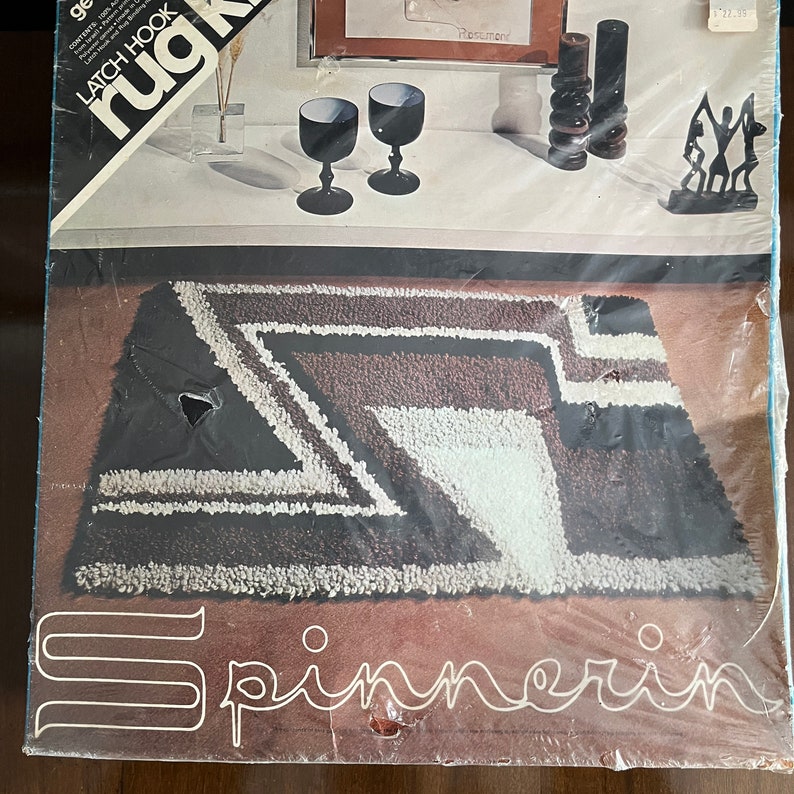 May include: A brown and white rug kit with the text "rug hook latch hook" and "Spinnerin" on the packaging. The rug kit features a geometric design with black, white, and brown yarn.