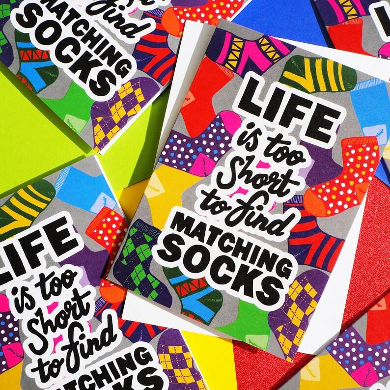 May include: Colorful greeting cards with a playful design featuring socks and the text "Life is too short to find matching socks".