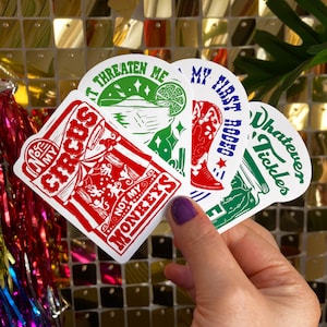 May include: Four colourful stickers with different designs. The first sticker is red and white with the text "Not My Circus, Not My Monkeys". The second sticker is green and white with the text "Whatever Tickles". The third sticker is blue and white with the text "My First Rodeo". The fourth sticker is green and white with the text "Threaten Me".