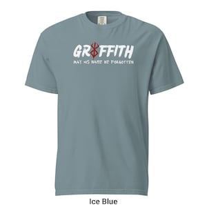 May include: A light blue t-shirt featuring a white graphic that reads "Griffith" with a red symbol above the word. The text below the graphic says "May his name be forgotten".