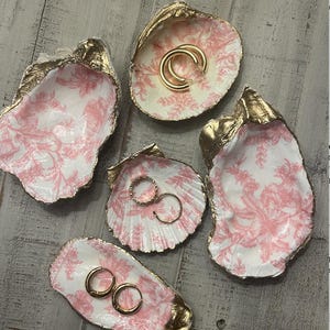 Op de afbeelding: Vijf decoratieve schelpvormige schalen met roze bloemenpatronen en gouden accenten. De schalen zijn perfect om sieraden of andere kleine voorwerpen in te bewaren.