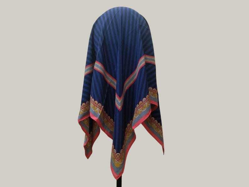 May include: A navy blue scarf with vertical stripes and decorative borders. The scarf has a repeating pattern of red, yellow, and blue accents along the edges. The scarf is draped over a stand, showcasing its design.