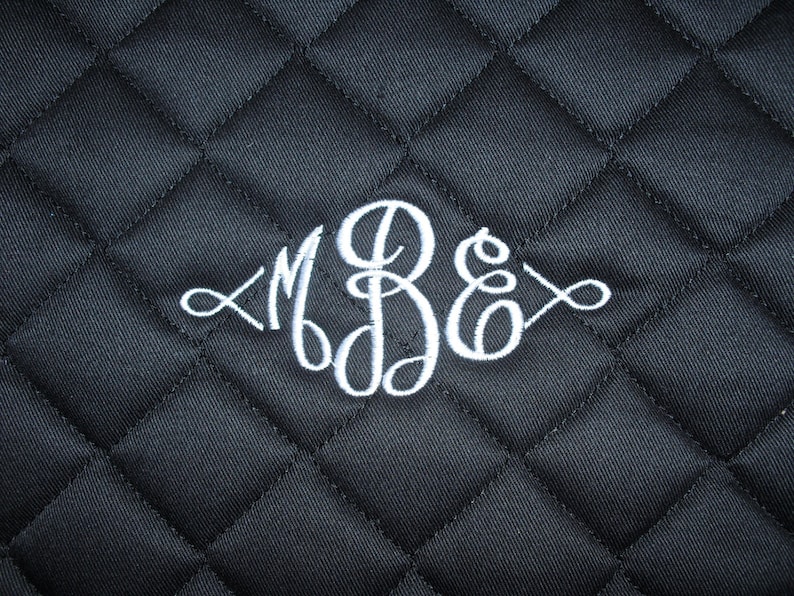 以下が含まれることがあります： 黒いキルティング生地に、白い刺繍で「MBE」の文字が筆記体で刺繍されています。