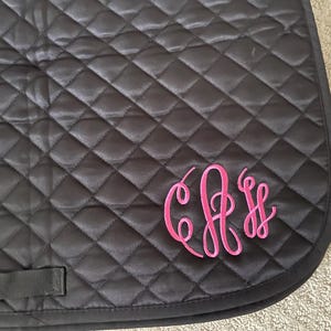 May include: Black quilted saddle pad with a pink monogram of the letters "C.F.S."