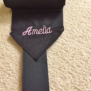 Puede incluir: Vendas negras para las piernas de caballo con un nombre bordado en rosa "Amelia" en una solapa triangular.