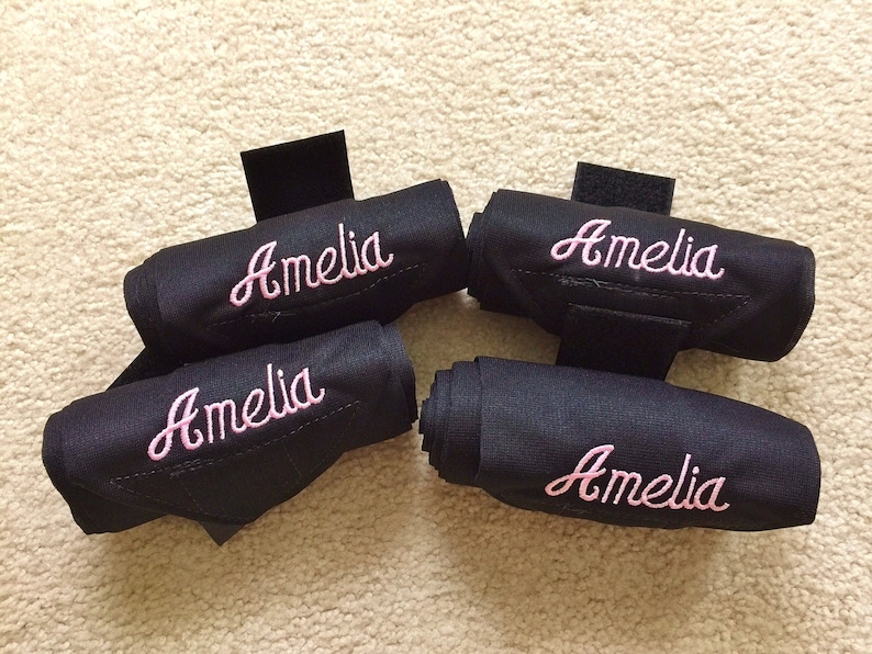 Puede incluir: Cuatro vendas negras para las piernas de caballo con bordado rosa que dice "Amelia".