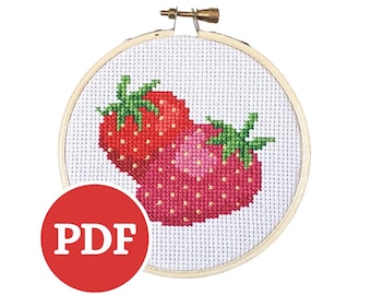 May include: A circular wooden embroidery hoop containing white Aida fabric with a cross-stitch pattern of two strawberries. The strawberries are rendered in shades of red and pink with green leaves. A red circular icon with the white text PDF is present.