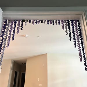 Peut inclure: Une porte est d&eacute;cor&eacute;e de brins de fil violets et bleus suspendus et en cascade, cr&eacute;ant un accent d&eacute;coratif de type floral. Les brins de fil sont de longueurs et de nuances variables, ajoutant de la profondeur et de l'int&eacute;r&ecirc;t visuel &agrave; l'espace. L'encadrement de la porte est blanc.