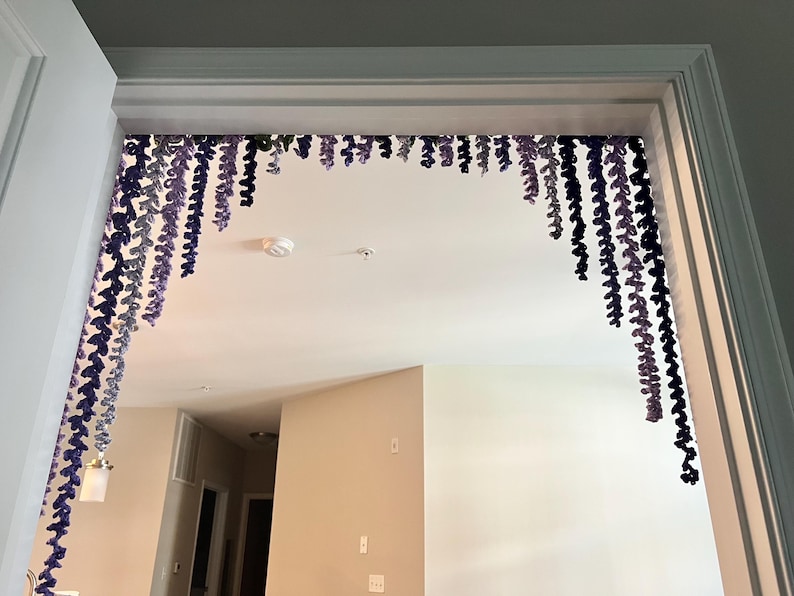 Peut inclure: Une porte est d&eacute;cor&eacute;e de brins de fil violets et bleus suspendus et en cascade, cr&eacute;ant un accent d&eacute;coratif de type floral. Les brins de fil sont de longueurs et de nuances variables, ajoutant de la profondeur et de l'int&eacute;r&ecirc;t visuel &agrave; l'espace. L'encadrement de la porte est blanc.