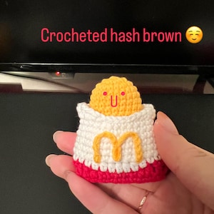May include: Crocheted hash brown in a red and white crocheted container with a yellow 'M' on the front. The hash brown has a happy face.