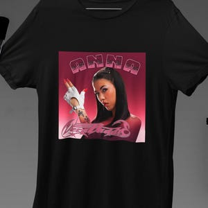 Könnte beinhalten: Schwarzes T-Shirt mit einem pinkfarbenen Grafikdruck einer Frau mit dem Text "ANNA" darüber. Die Grafik enthält ein pinkfarbenes und weißes Skorpion-Design.