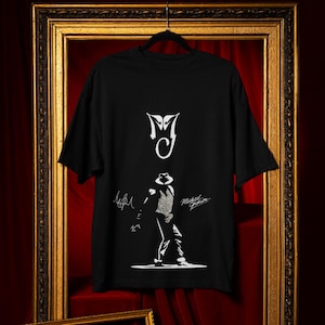 Op de afbeelding: Zwart T-shirt met een wit silhouet van Michael Jackson, het "MJ"-logo en zijn handtekening.