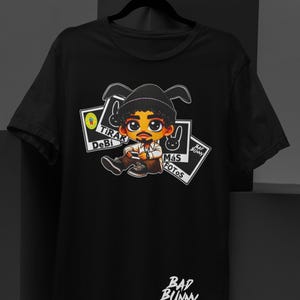 May include: Black t-shirt featuring a cartoon illustration of a person with a hat and holding a phone. The shirt has the text "Tirar Debi M&aacute;s Fotos" and "Bad Bunny" in white.