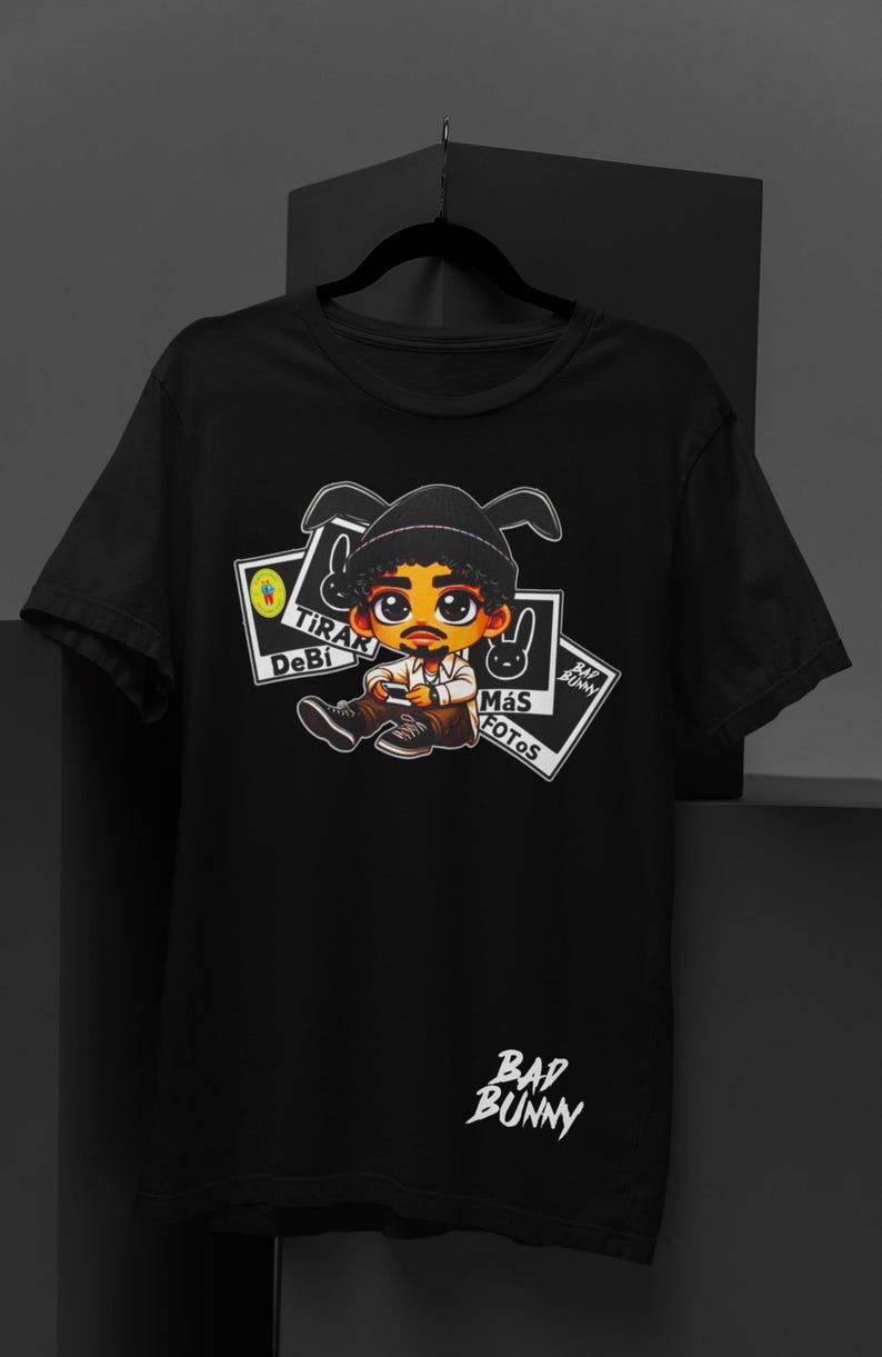 May include: Black t-shirt featuring a cartoon illustration of a person with a hat and holding a phone. The shirt has the text "Tirar Debi M&aacute;s Fotos" and "Bad Bunny" in white.