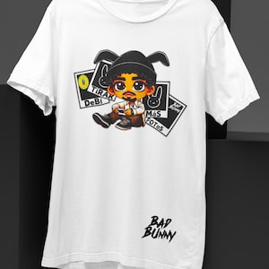 May include: White t-shirt featuring a cartoon illustration of a person with a black hat and mustache. The shirt has the text "BAD BUNNY" in black script and several graphic elements with text in Spanish.