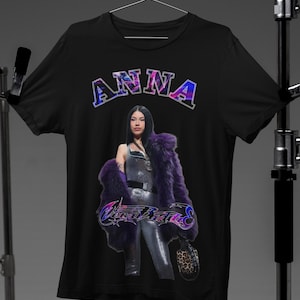 Könnte beinhalten: Schwarzes T-Shirt mit einem lila und blauen Grafikdruck einer Frau, die einen lila Pelzmantel und ein silbernes Outfit trägt. Der Text "ANNA" befindet sich über der Frau und der Text "West Blvd" unter ihr.