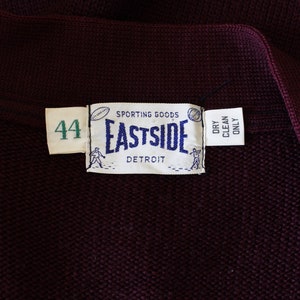 May include: Close-up of a dark burgundy knit garment with a label that reads "SPORTING GOODS EASTSIDE DETROIT". The label also includes the number "44" and the words "DRY CLEAN ONLY".