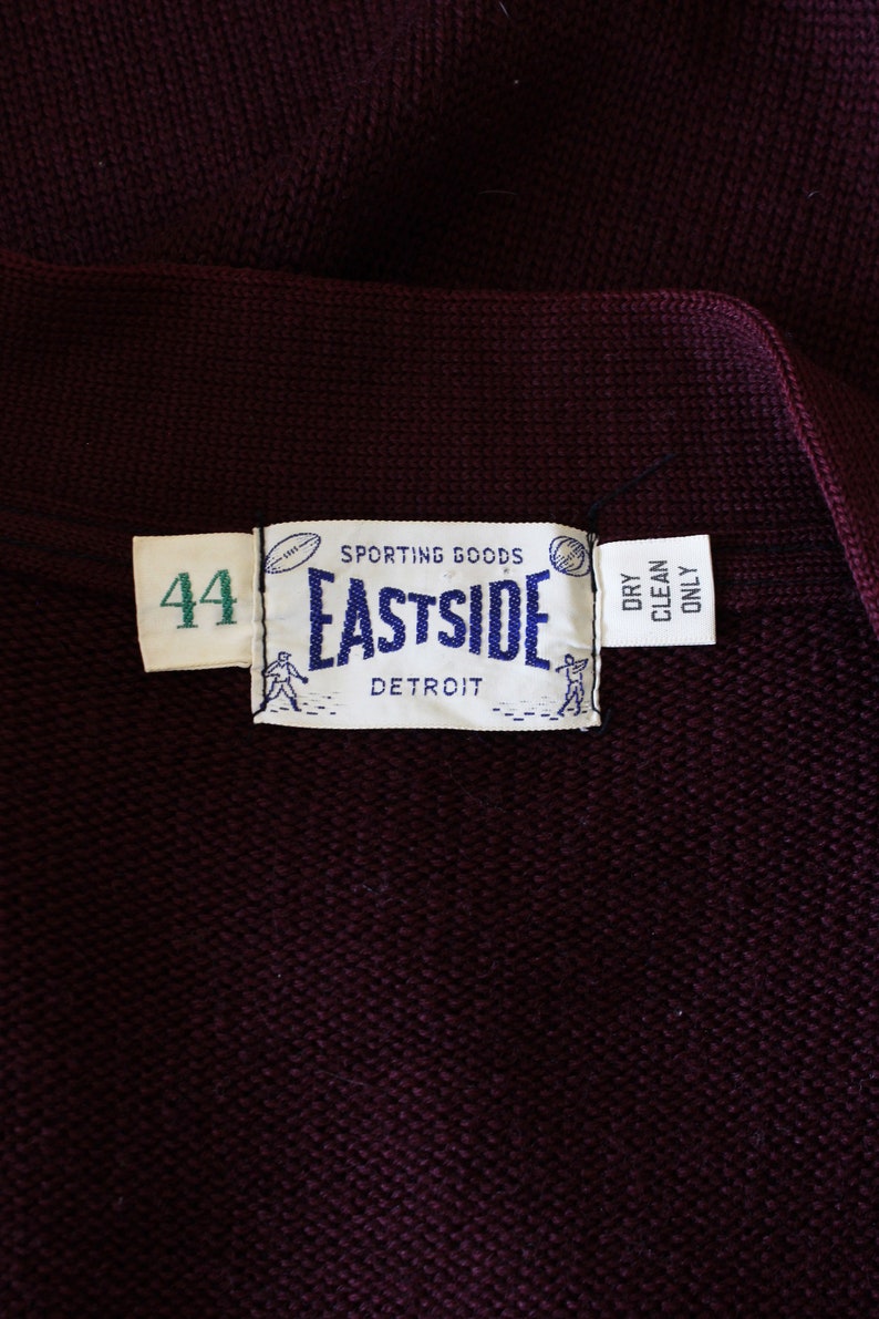 May include: Close-up of a dark burgundy knit garment with a label that reads "SPORTING GOODS EASTSIDE DETROIT". The label also includes the number "44" and the words "DRY CLEAN ONLY".