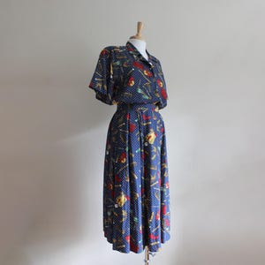 May include: A blue and white patterned dress with a short-sleeved top and a long skirt. The dress has a white polka dot pattern and a colourful print of various objects.