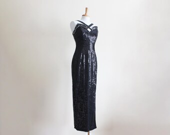 May include: A black sequined evening gown displayed on a mannequin. The dress features a fitted bodice with embellished straps and a floor-length skirt. The sequins create a shimmering effect, perfect for formal events.