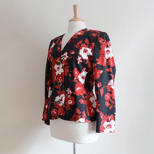 May include: A black blazer with a vibrant red and white floral pattern. The jacket features long sleeves, a V-neck, and gold-colored buttons. The garment is displayed on a mannequin.