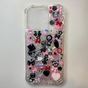 May include: A clear phone case with a black and pink design. The case is decorated with various charms, including stars, bows, hearts, and cartoon characters.