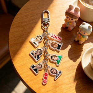May include: A silver keychain with multiple clear acrylic charms featuring images of a person. The keychain includes a charm with the name "JIMIN" in red letters. Additional charms are red and white.