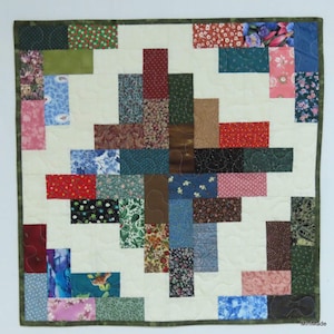 May include: A patchwork quilt with a geometric design featuring a variety of colourful fabrics. The quilt is made up of squares and rectangles of different sizes and colours, creating a visually interesting pattern. The quilt is edged with a green border.