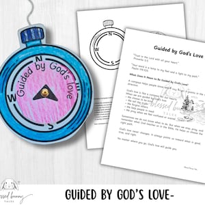 Puede incluir: Un adorno de brújula azul y rosa con las palabras "Guided by God's Love". La brújula tiene una aguja negra y un cordón plateado para colgar. También se ven dos páginas blancas con texto y una ilustración de brújula.