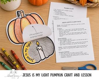 May include: A paper pumpkin craft with a lift-the-flap feature revealing a candle illustration and the text 'Jesus is my light'. Beside it are printed instruction sheets titled 'Pumpkin Craft' and 'Jesus Lights a Light in Us', along with crayons and scissors.
