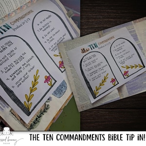 May include: A white paper Bible tip-in featuring a hand-drawn illustration of two stone tablets containing The Ten Commandments, Exodus 20:1-17. The design includes black ink text, yellow leafy branches, and pink flowers, set against a printed Bible page.