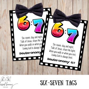 May include: Two white tags with black borders and a black bow tie on top. The tags feature the numbers "6:7" in colorful text, with the text "Six-seven, day and night" and "Deuteronomy 6:7". The words "SIX-SEVEN TAGS" are at the bottom.