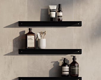 May include: Three matte black metal wall shelves arranged vertically. The top shelf holds a white tube and a brown spray bottle. The middle shelf features a brown bottle, a white cup, and two toothbrushes. The bottom shelf holds two brown pump bottles.