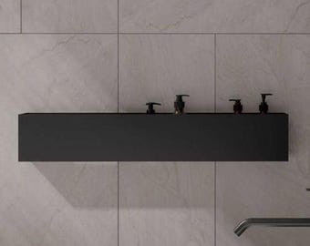 May include: A matte black rectangular wall-mounted shelf holding four small pump bottles, positioned above a white oval bathtub. A tall matte black floor-mounted faucet with a handheld shower attachment stands beside the bathtub.