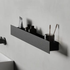 May include: A black metal shelf with rounded edges mounted to a wall. The shelf is holding various toiletries, including a tube of toothpaste, bottles of shampoo, and a toothbrush holder.