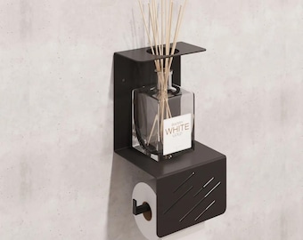 May include: Black metal wall-mounted toilet paper holder with a shelf for a diffuser bottle and reeds. The shelf has a black metal frame and a black patterned design. The toilet paper holder has a white roll of toilet paper.
