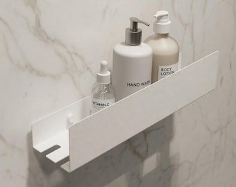 Puede incluir: Un estante de pared de metal blanco mate que sostiene tres botellas. Las botellas incluyen un frasco cuentagotas de vidrio transparente con la etiqueta Vitamin C, una botella con dosificador blanca con la etiqueta Hand Wash y otra con Body Lotion.
