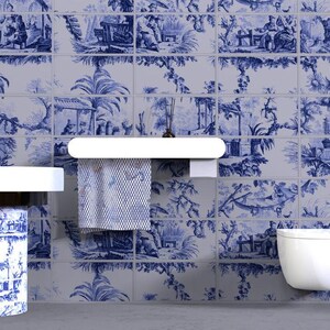May include: A wall covered in rectangular tiles featuring a blue and white toile pattern depicting pastoral scenes with figures, trees, and structures. A white shelf holds a patterned towel, and a white sink and toilet are visible.