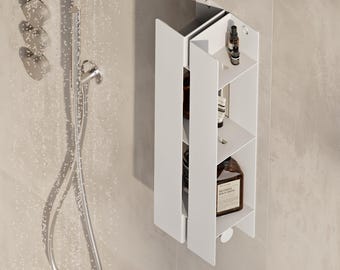 May include: A white vertical shower caddy with three shelves mounted on a tiled wall. The caddy features a slim, angular design with open sides, holding various dark-colored toiletry bottles. A chrome shower head and controls are visible nearby.