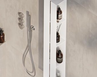 May include: A tall, vertical white shower shelf unit with four open compartments. The shelves hold various amber-colored bottles, a reed diffuser, and a tube. A round wooden brush hangs from a hook at the bottom of the white metal storage unit.
