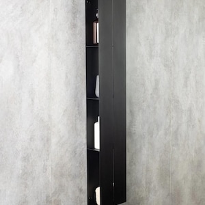 以下が含まれることがあります： 2つのドアが付いた、背の高い黒い壁掛けキャビネット。キャビネットには、ボトルやスポンジなど、さまざまなバスルーム製品を収納できる棚がいくつかあります。キャビネットは、グレーのテクスチャード加工された壁に設置されています。