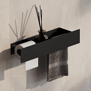 Può includere: Una mensola da bagno a parete in nero opaco con portarotolo integrato sul lato sinistro e un piano d'appoggio sulla destra. Un piccolo diffusore in vetro con bastoncini neri è posizionato sulla mensola accanto a un asciugamano grigio appeso.