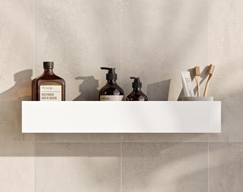May include: A long, rectangular white wall shelf holding an amber glass mouthwash bottle with a label reading Aesop Mouthwash, two amber glass pump bottles with Aesop labels, a tube of toothpaste, and two wooden toothbrushes in a grey cup.