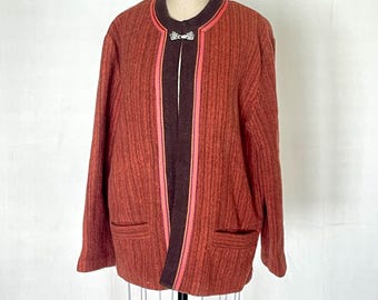 May include: A vintage rust-colored jacket with a textured weave, featuring a dark brown collar and trim. The jacket has a coral-colored accent stripe along the open front and pockets. A decorative clasp secures the front. The jacket is displayed on a mannequin.