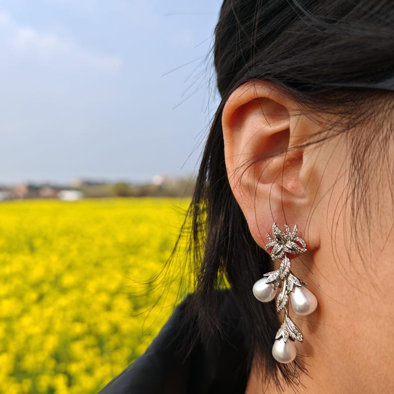 May include: Silver dangle earrings with a floral design and pearl accents.