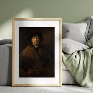 May include: Framed print of a classic portrait. The artwork depicts a man in a dark hat and brown coat, with a somber expression. The painting is set against a dark background, and the frame is a light wood color.