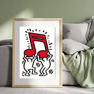 May include: Framed art print depicting a red musical note held by two white figures with black outlines. The artwork is in a pop art style, with bold lines and a minimalist design. The frame is a light wood colour.
