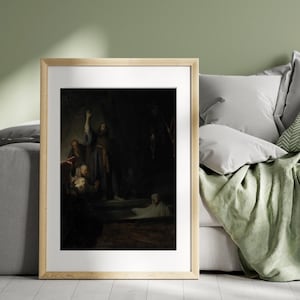 May include: Framed print of a dark, dramatic painting. A figure in a long robe raises an arm, illuminated by a light source. Other figures are gathered below, with a sense of mystery and depth. The frame is a light wood color.
